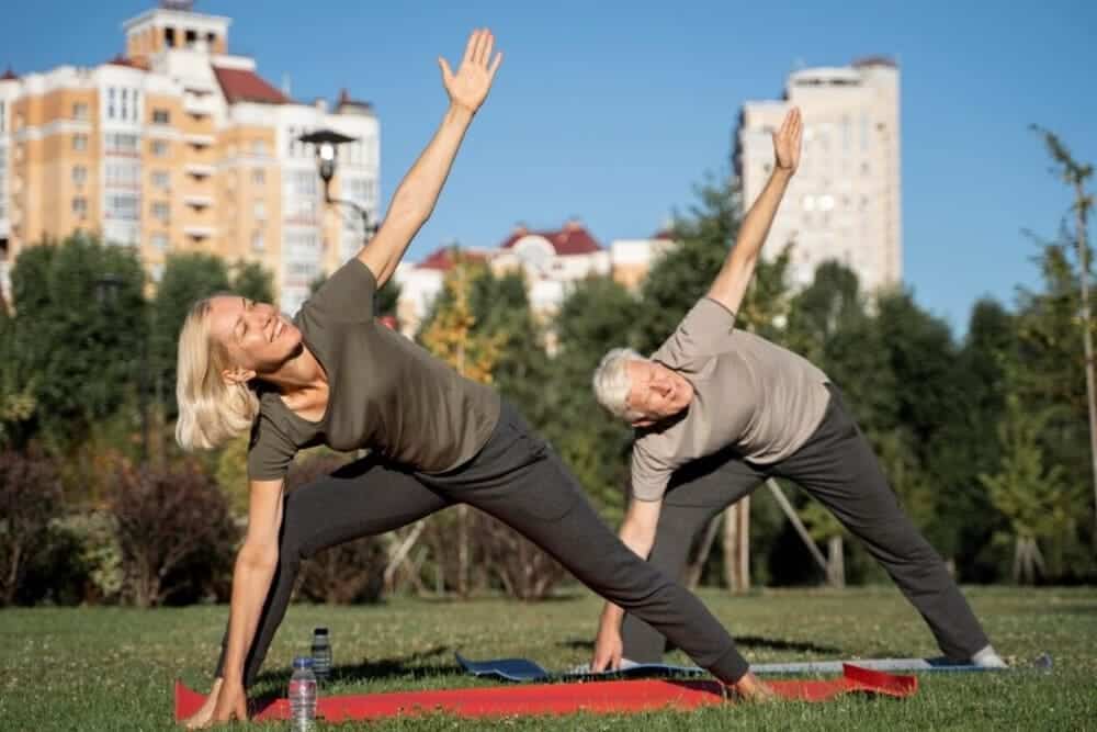 vista lateral pareja ancianos practicando yoga al aire libre